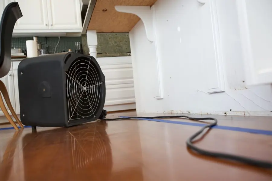 Air mover drying a wood floor under a kitchen counter overhang after a leak