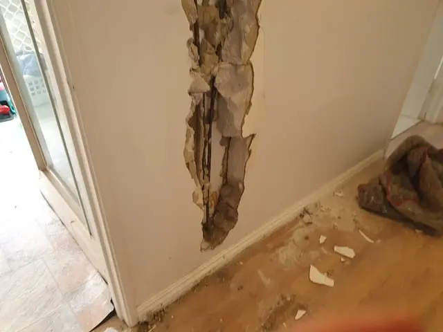 Wall opened at a doorway with drywall debris on the floor after a leak