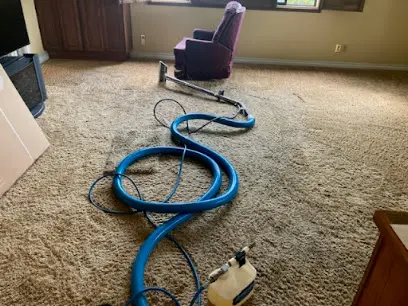Extraction hose and wand laid across wet carpet in a living room during water removal